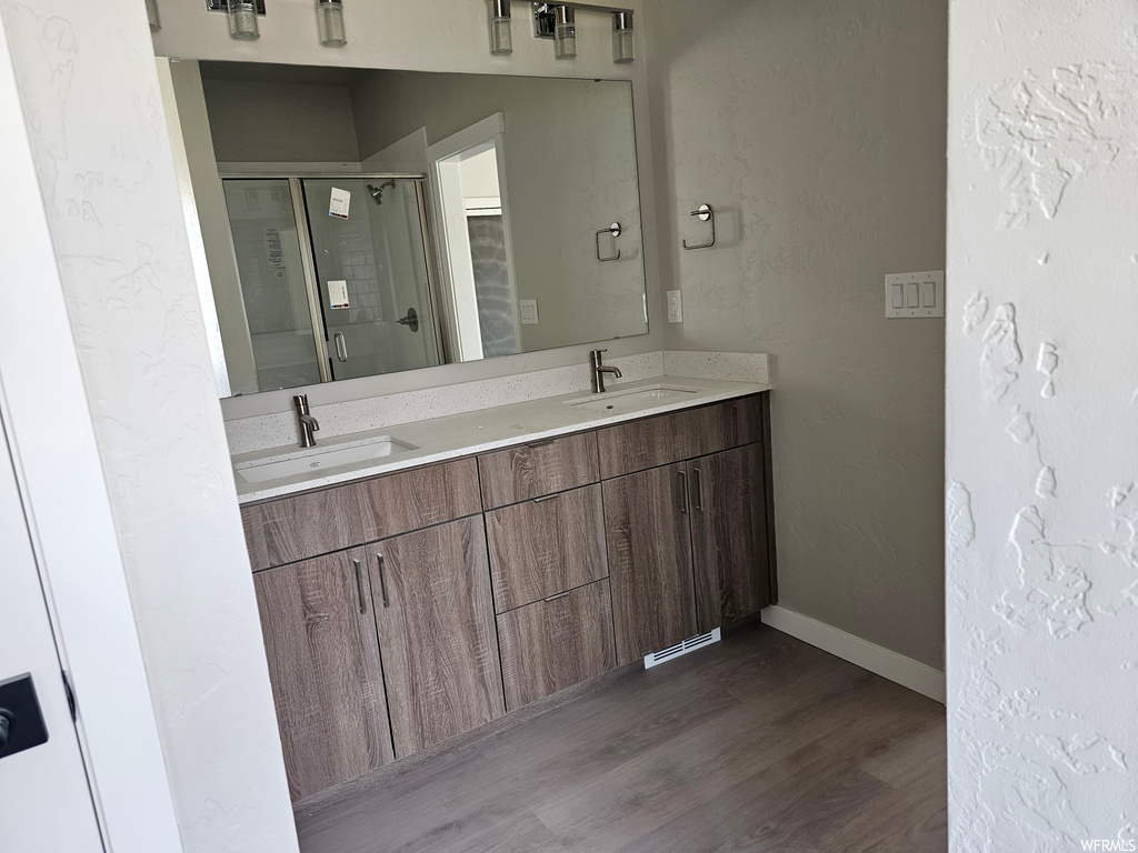 Bathroom with a shower with shower door, dark hardwood flooring, double vanity, and mirror