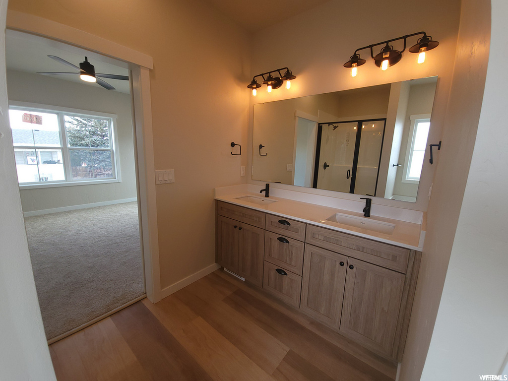 Bathroom with wood-type flooring, natural light, a ceiling fan, double sink vanity, mirror, and shower with glass door