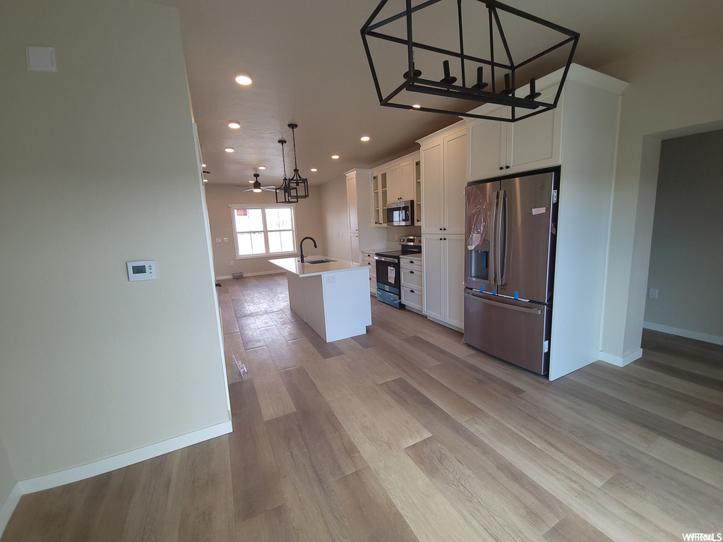 Kitchen featuring a ceiling fan, natural light, refrigerator, range oven, stainless steel microwave, white cabinets, light parquet floors, and kitchen island sink