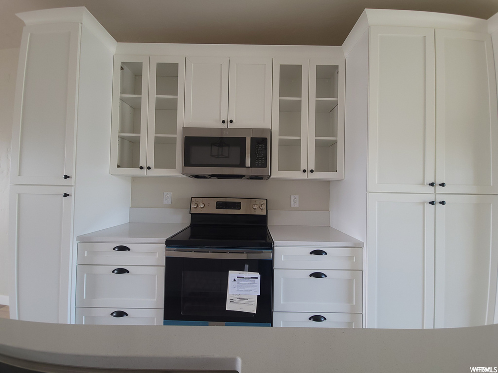 Kitchen with electric range oven, microwave, and white cabinetry