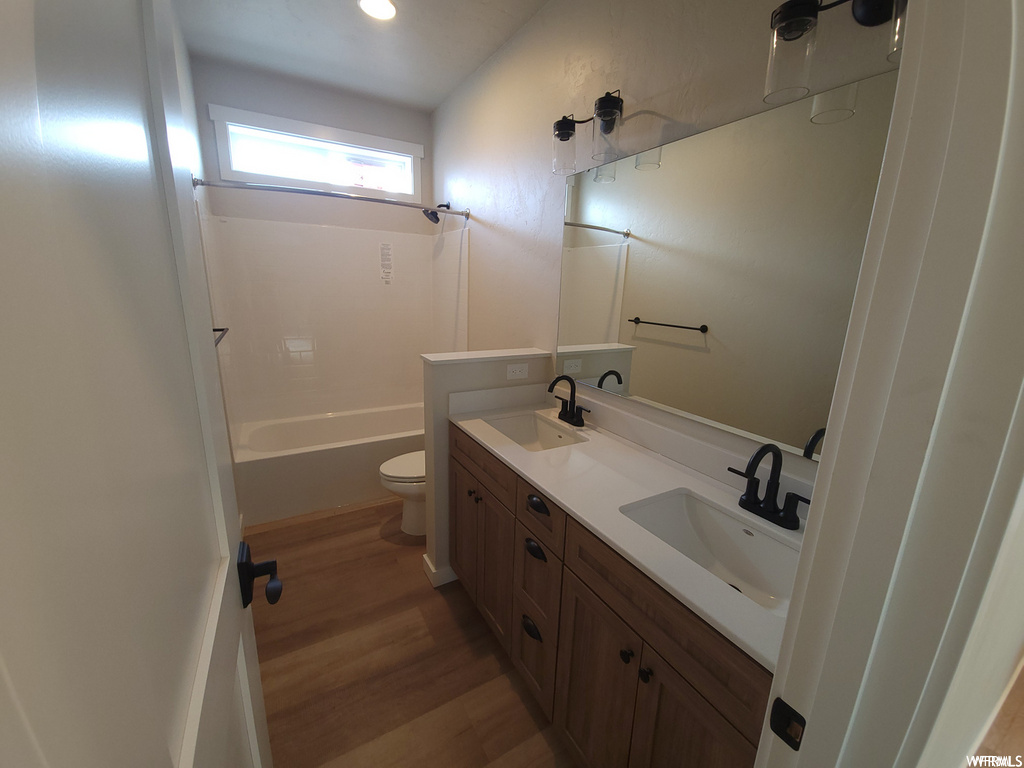 Full bathroom featuring wood-type flooring, natural light, toilet, mirror, dual bowl vanity, and bathtub / shower combination