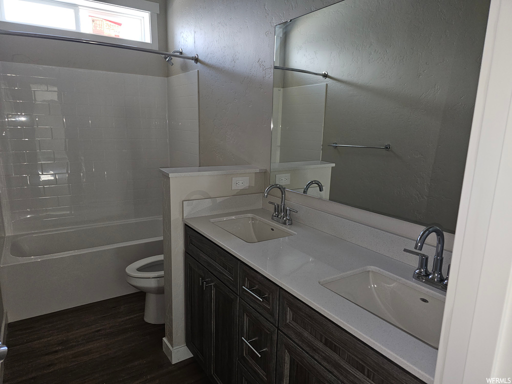 Full bathroom with mirror, dark parquet floors, dual large vanity, and washtub / shower combination