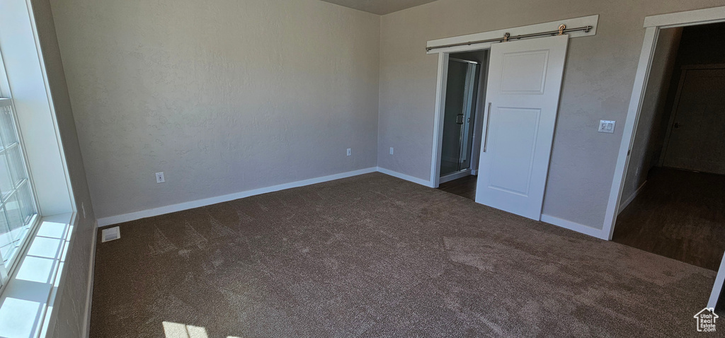 Unfurnished bedroom featuring dark carpet and a barn door
