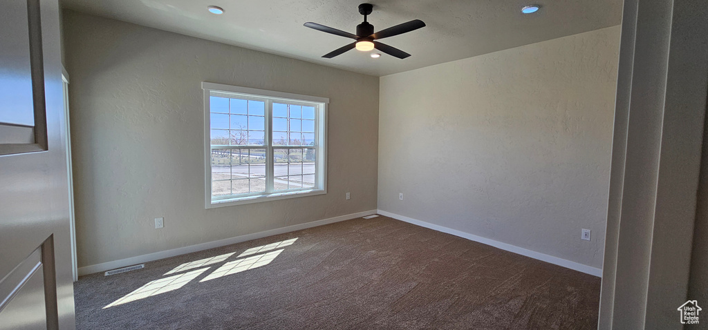 Empty room with ceiling fan and dark colored carpet