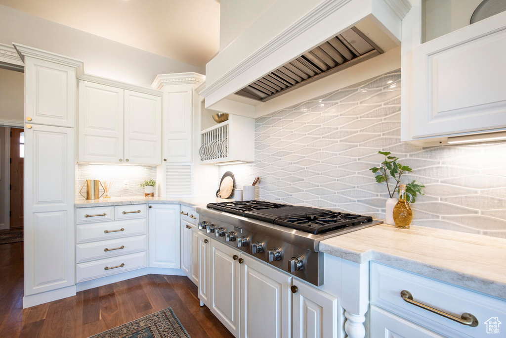 Kitchen with custom range hood, white cabinets, dark hardwood / wood-style floors, and backsplash