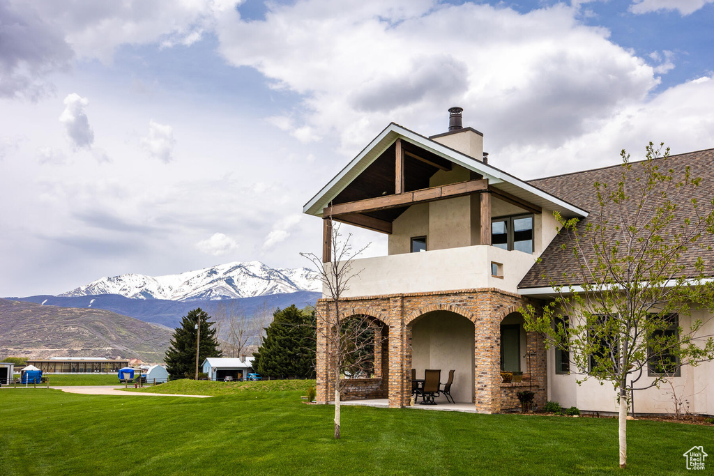 Rear view of house featuring a balcony, a lawn, a mountain view, and a patio