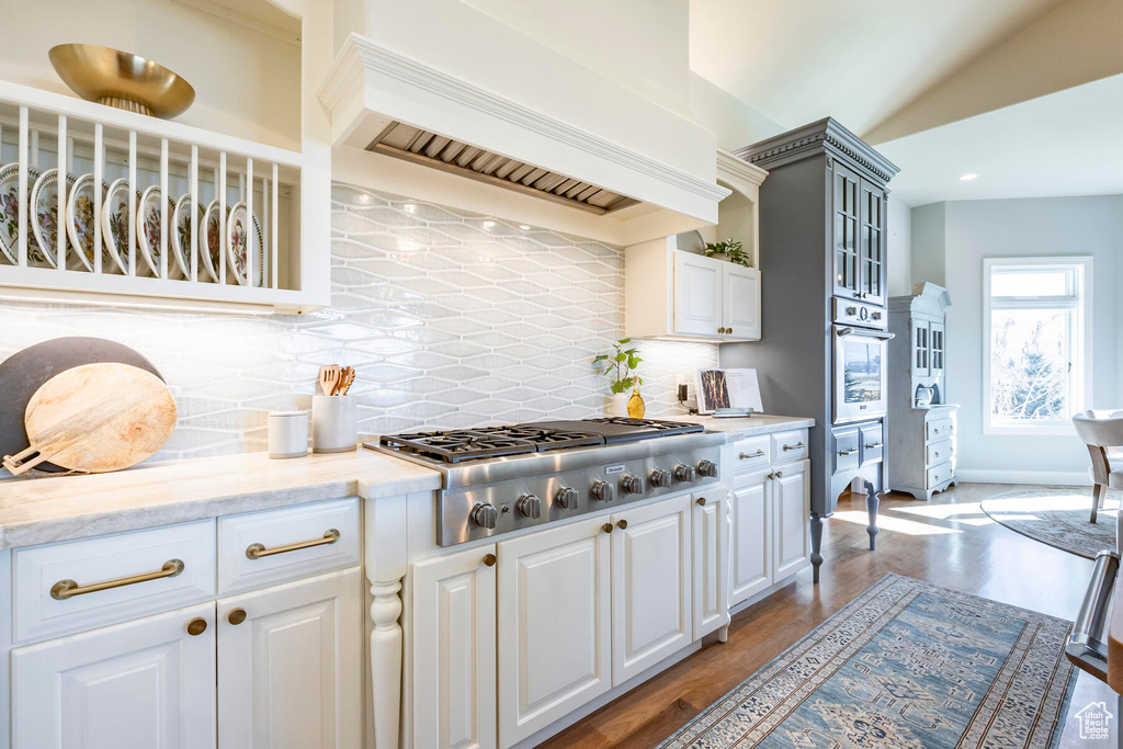 Kitchen featuring light hardwood / wood-style floors, custom range hood, light stone counters, stainless steel gas stovetop, and tasteful backsplash