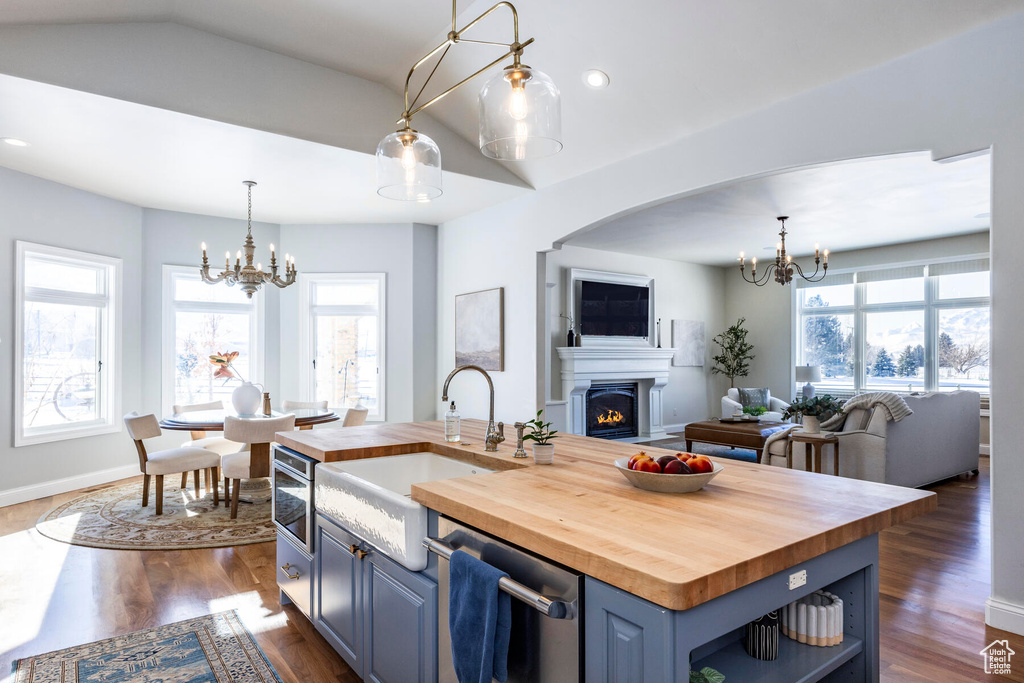 Kitchen featuring blue cabinets, an inviting chandelier, a center island with sink, and butcher block counters