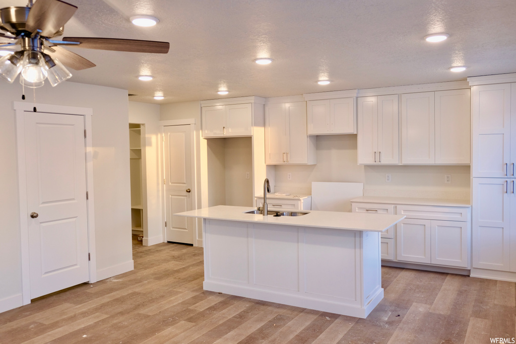 kitchen with a kitchen island, a ceiling fan, light parquet floors, light countertops, and white cabinets