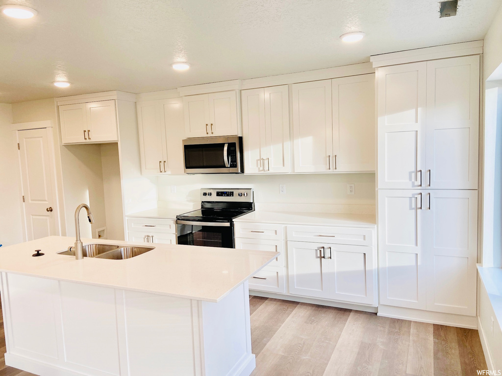 Kitchen featuring microwave, electric range oven, white cabinets, light countertops, and light hardwood flooring