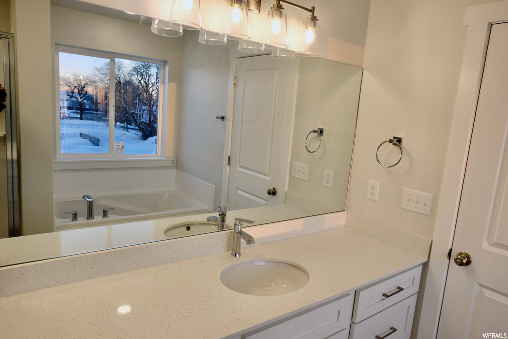 bathroom featuring natural light, mirror, large vanity, and a bathtub