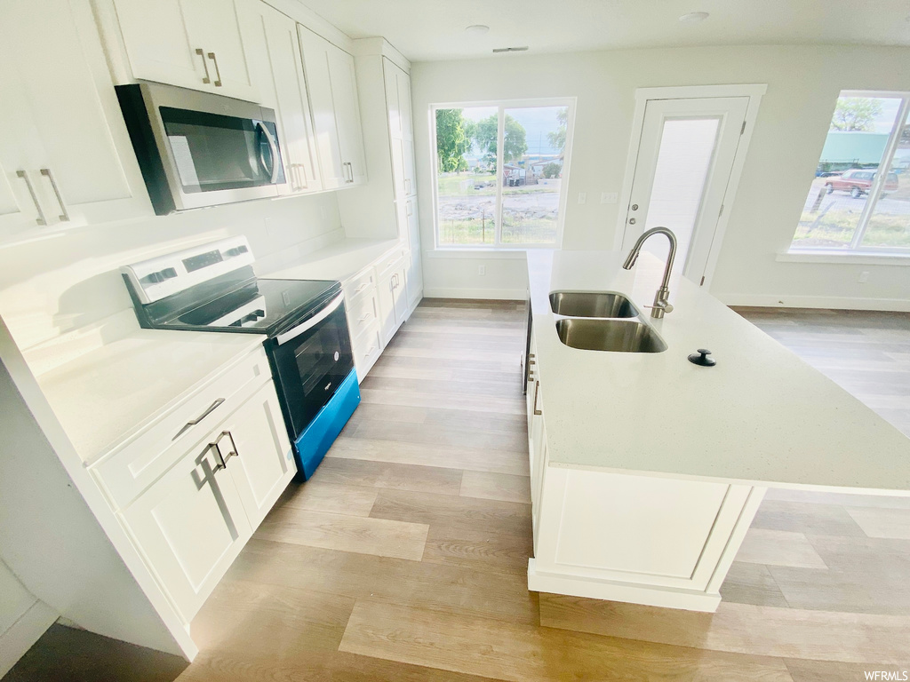 Kitchen featuring natural light, electric range oven, microwave, and light hardwood floors