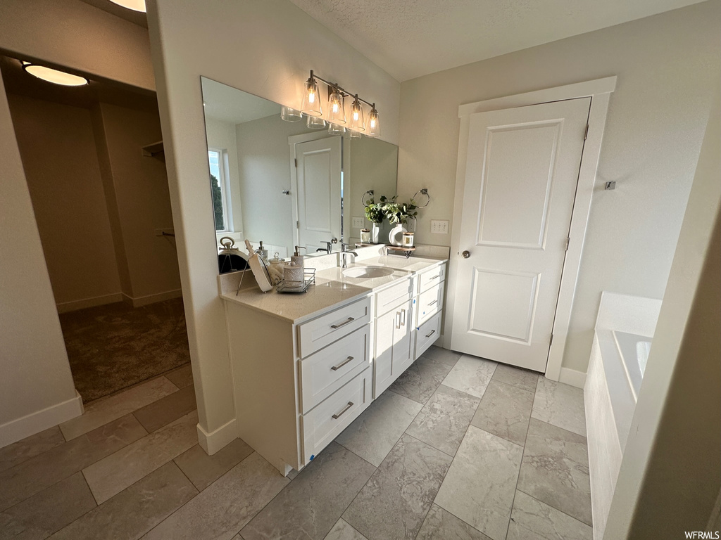 Bathroom featuring mirror, double sink vanity, a bath to relax in, and light tile floors