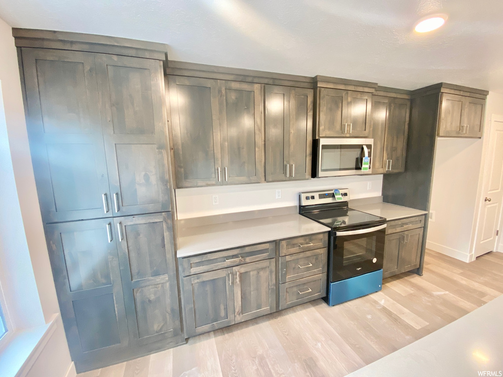 Kitchen with electric range oven, microwave, light countertops, and light parquet floors