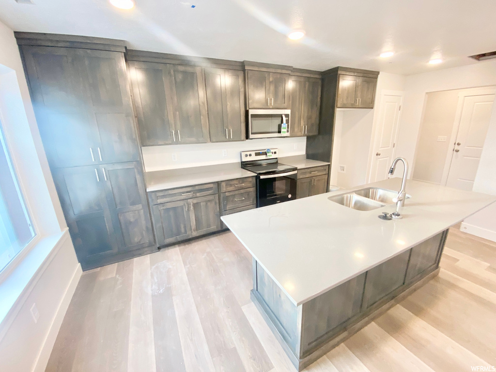 Kitchen featuring microwave, electric range oven, light hardwood flooring, and light countertops