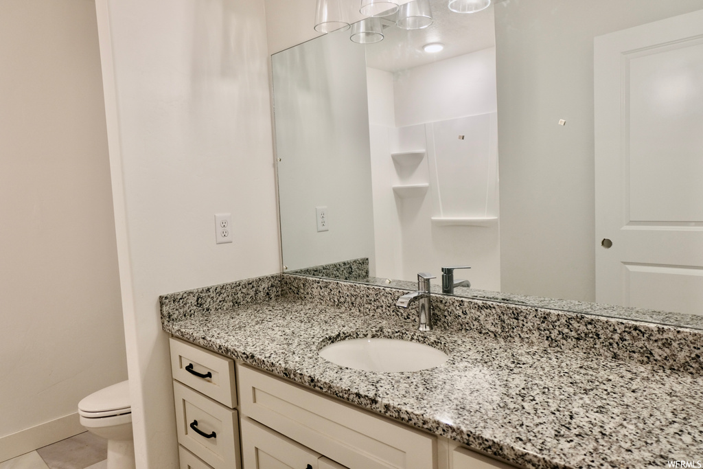 half bathroom with tile floors, mirror, vanity with extensive cabinet space, and toilet