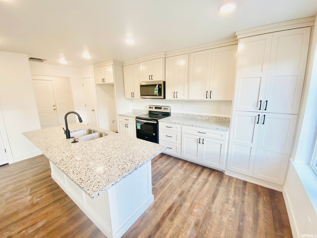 Kitchen with microwave, electric range oven, kitchen island sink, light stone countertops, light parquet floors, and white cabinetry