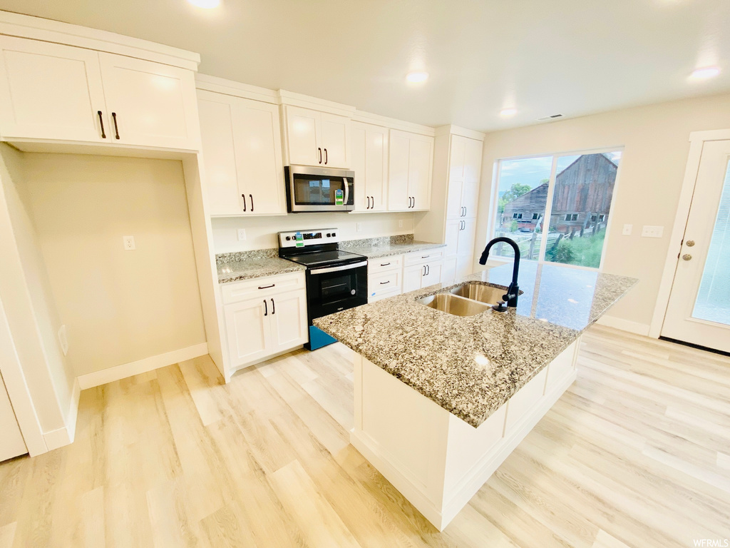 Kitchen with natural light, microwave, electric range oven, granite-like countertops, white cabinetry, and light hardwood floors