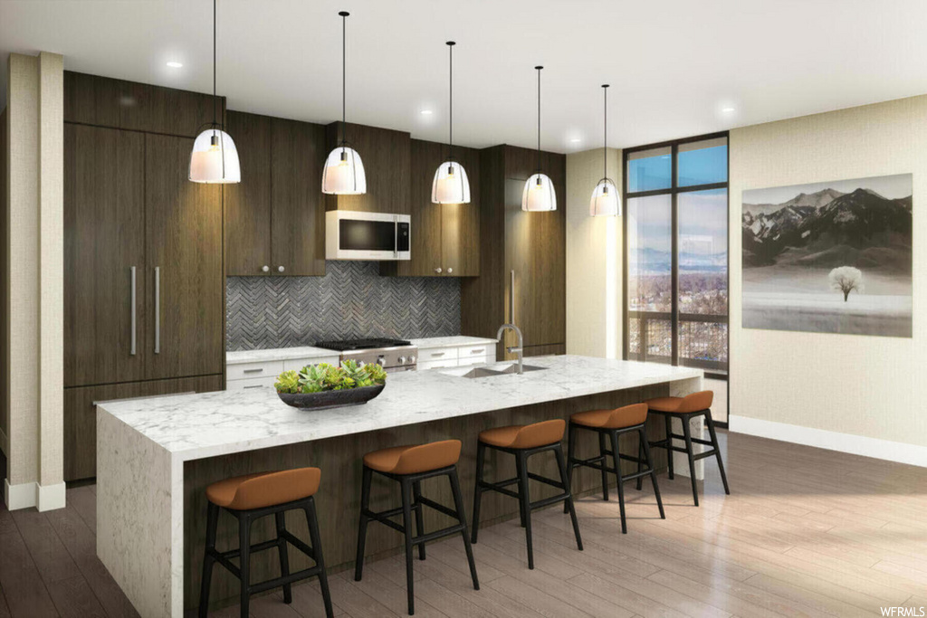 kitchen with natural light, a breakfast bar, wood-type flooring, range oven, microwave, kitchen island sink, light granite-like countertops, and pendant lighting