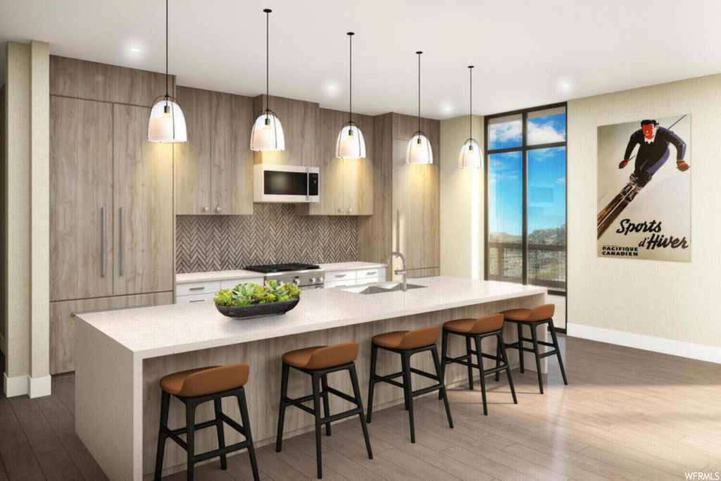 kitchen featuring natural light, a breakfast bar, wood-type flooring, microwave, light countertops, kitchen island sink, and pendant lighting