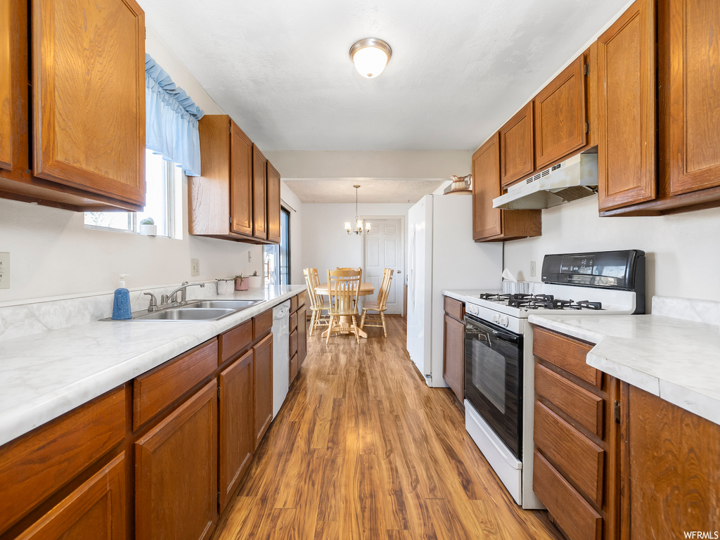 kitchen featuring natural light, fume extractor, dishwasher, gas range oven, brown cabinetry, light countertops, and light hardwood floors