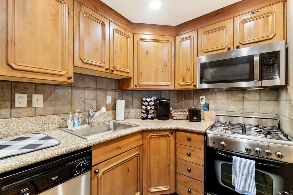 kitchen with microwave, dishwasher, gas range oven, brown cabinets, and light granite-like countertops