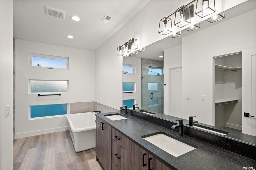 Bathroom with dual bowl vanity, mirror, light hardwood flooring, and shower with separate bathtub