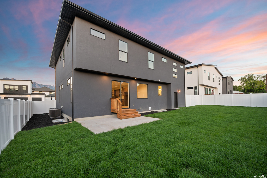 Back house at dusk featuring a yard and a patio area