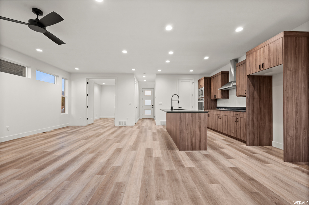 Kitchen with ceiling fan, wall chimney range hood, and light hardwood flooring