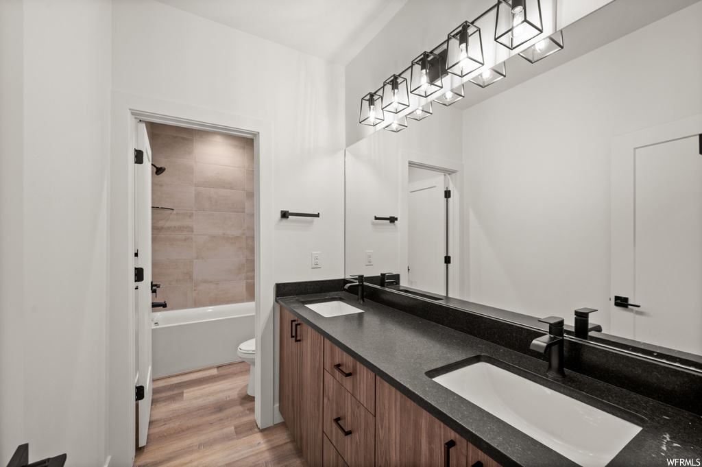 Full bathroom featuring double large sink vanity, tiled shower / bath, mirror, and light hardwood floors