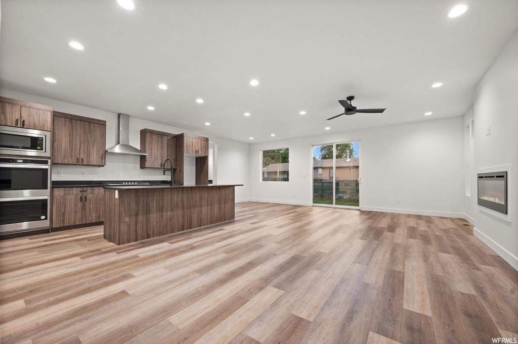 Kitchen featuring ceiling fan, wall chimney range hood, appliances with stainless steel finishes, and light parquet floors