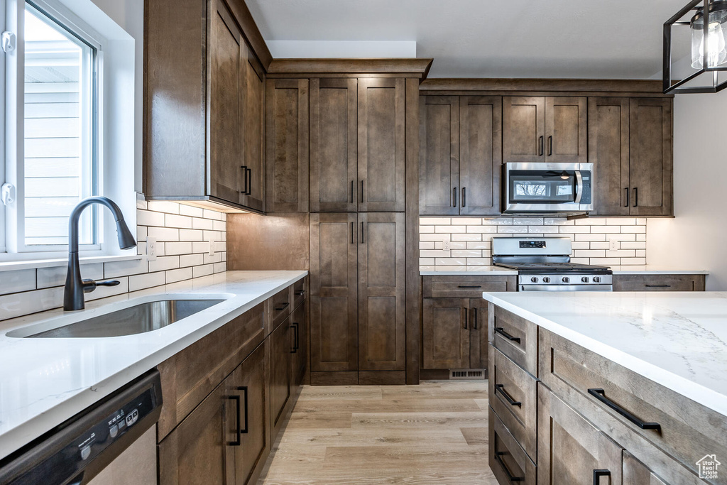 Kitchen featuring dark brown cabinetry, light hardwood / wood-style flooring, tasteful backsplash, and stainless steel appliances