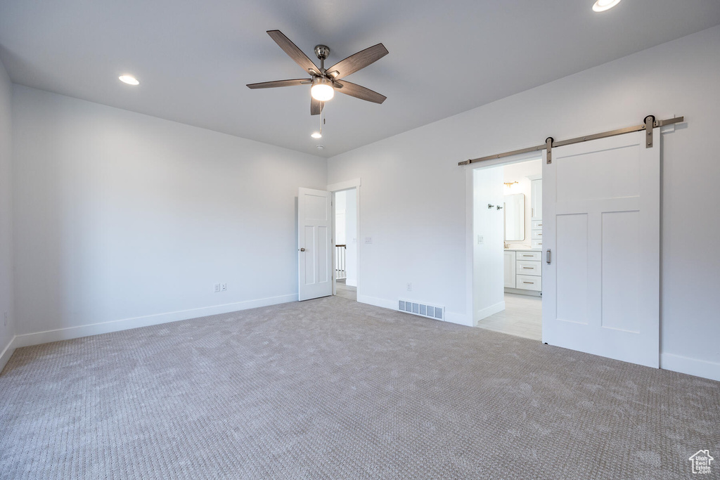 Unfurnished bedroom with a barn door, connected bathroom, light colored carpet, and ceiling fan
