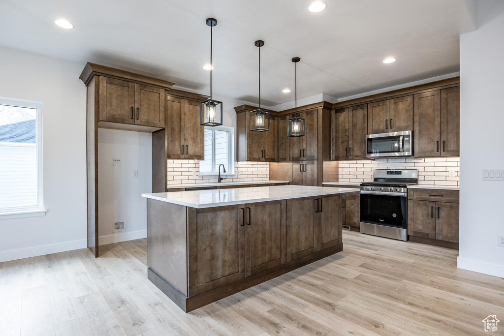 Kitchen featuring hanging light fixtures, light wood-type flooring, appliances with stainless steel finishes, and backsplash