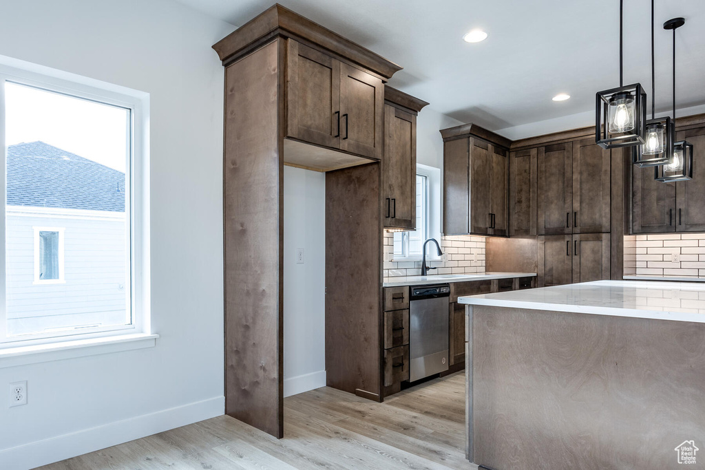 Kitchen featuring hanging light fixtures, stainless steel dishwasher, backsplash, light wood-type flooring, and dark brown cabinets