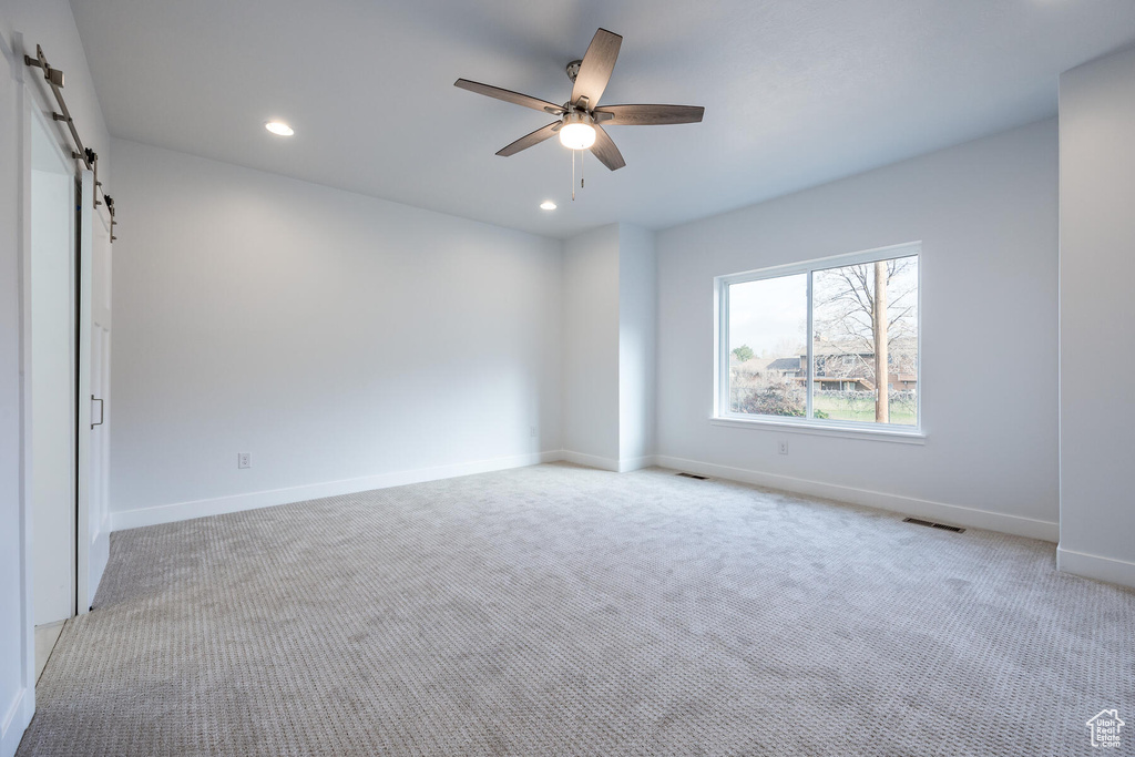 Spare room featuring light carpet, a barn door, and ceiling fan
