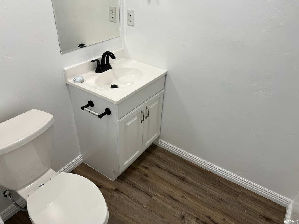 half bath featuring wood-type flooring, mirror, vanity, and toilet