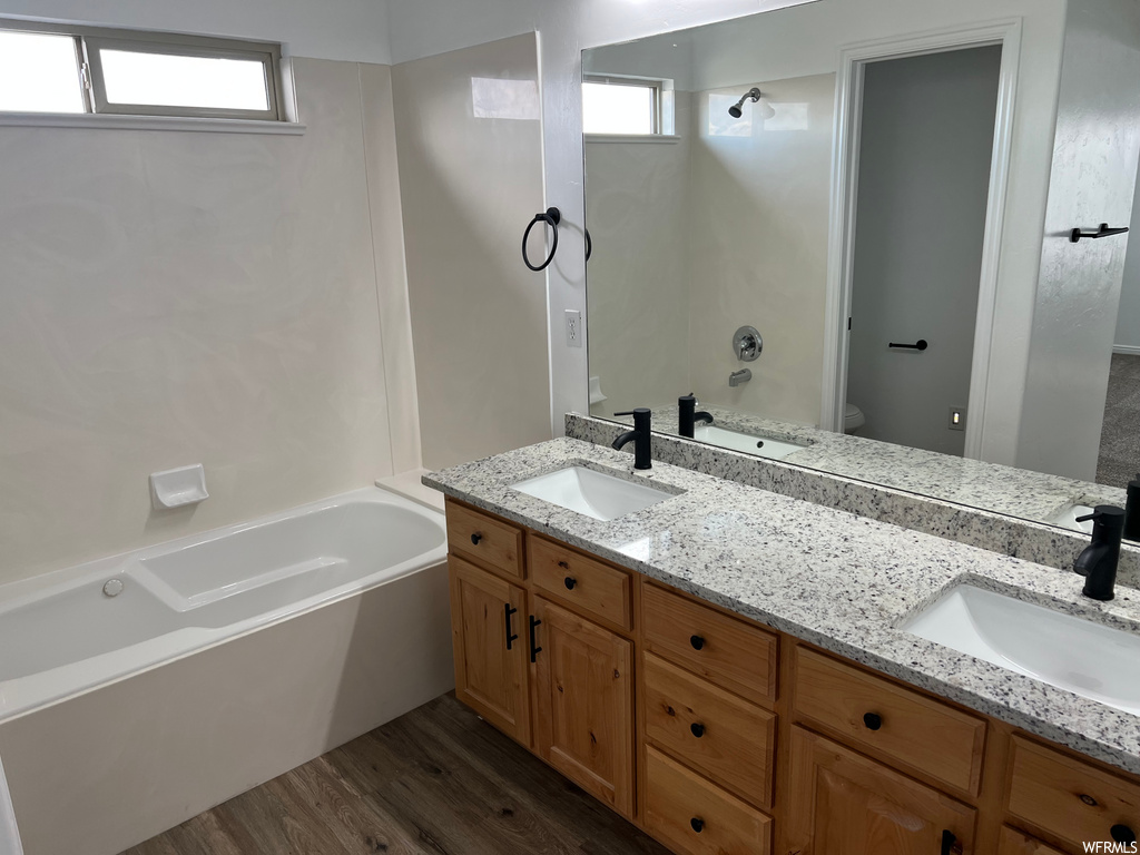 full bathroom with natural light, wood-type flooring, shower / bathing tub combination, mirror, dual bowl vanity, and toilet