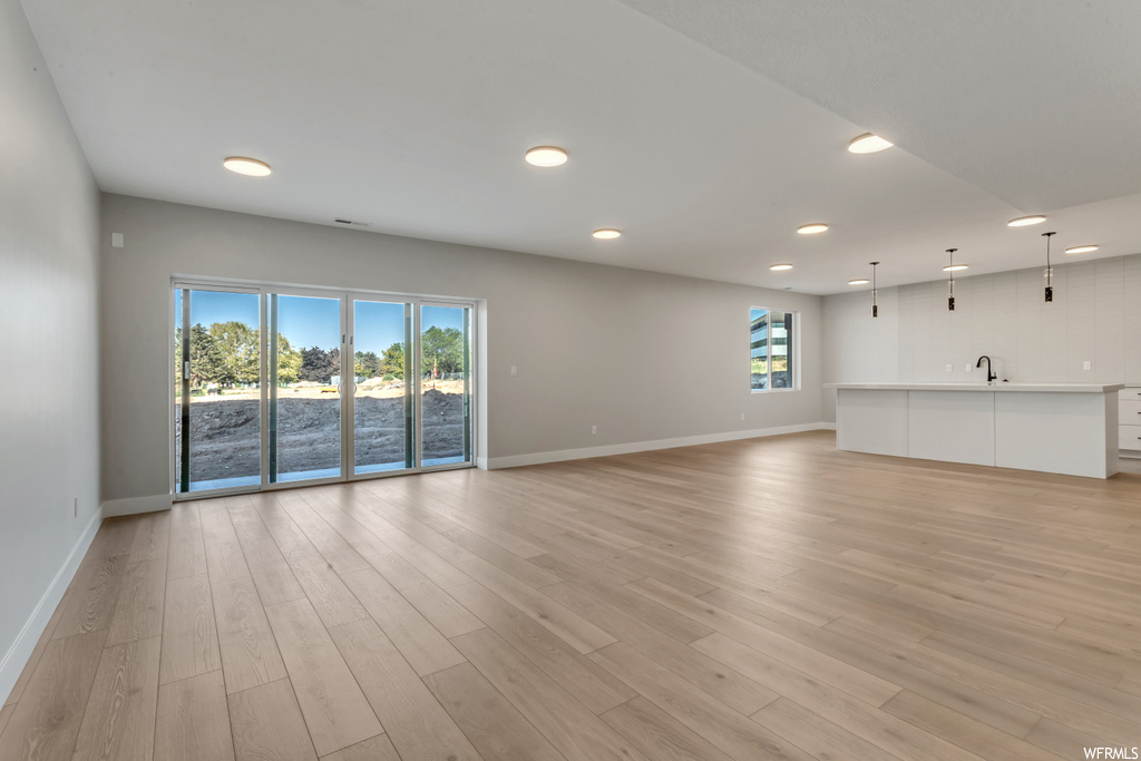 Unfurnished living room featuring light hardwood floors, sink, and a wealth of natural light