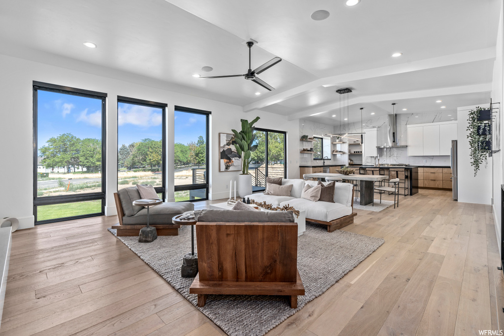 hardwood floored living room featuring natural light, a kitchen bar, and a ceiling fan