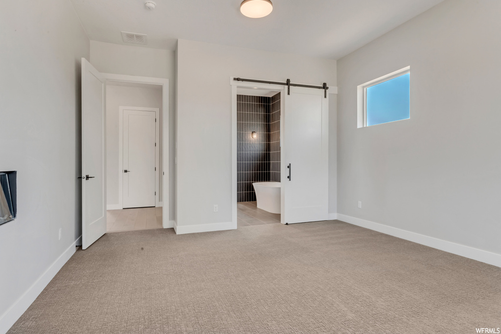 Unfurnished bedroom with a barn door, connected bathroom, and light colored carpet