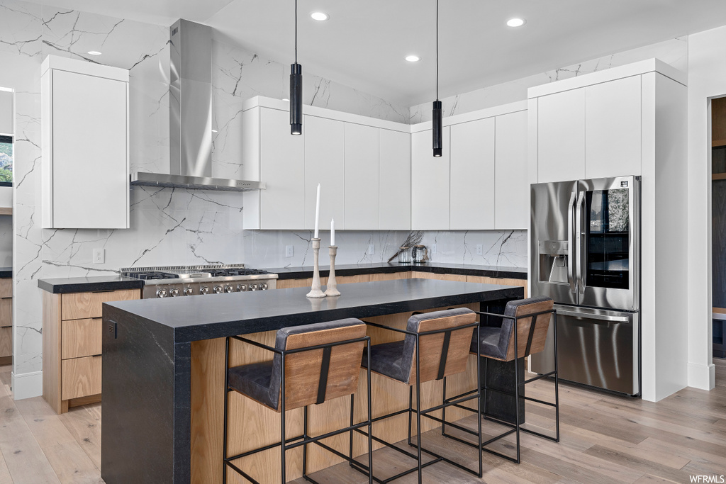 kitchen featuring a breakfast bar, fume extractor, gas stovetop, refrigerator, pendant lighting, and light hardwood floors