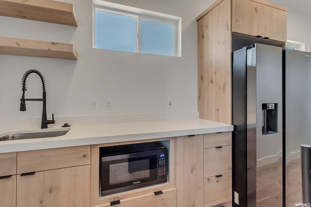 Kitchen featuring black microwave, sink, light hardwood / wood-style floors, stainless steel fridge, and light brown cabinetry
