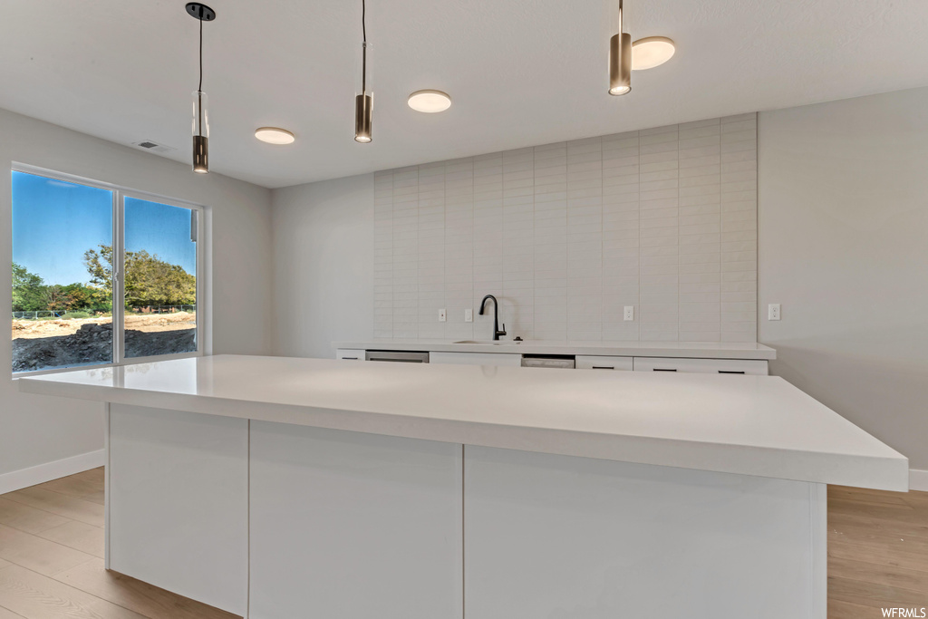 Kitchen featuring white cabinets, light hardwood flooring, a kitchen island, hanging light fixtures, and tasteful backsplash
