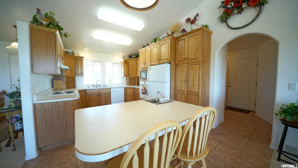 kitchen with oven, microwave, refrigerator, dishwasher, brown cabinets, light countertops, and light tile floors