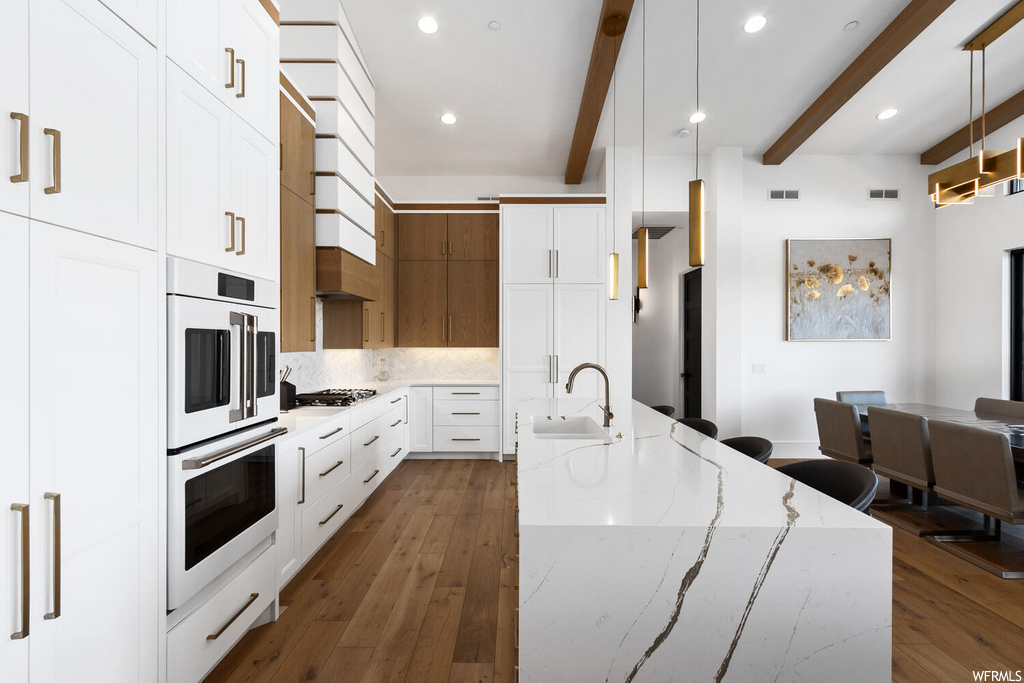 kitchen featuring stainless steel double oven, gas cooktop, light countertops, kitchen island sink, light parquet floors, and pendant lighting