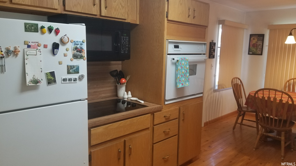 kitchen featuring refrigerator, electric stovetop, microwave, oven, light hardwood flooring, and brown cabinets