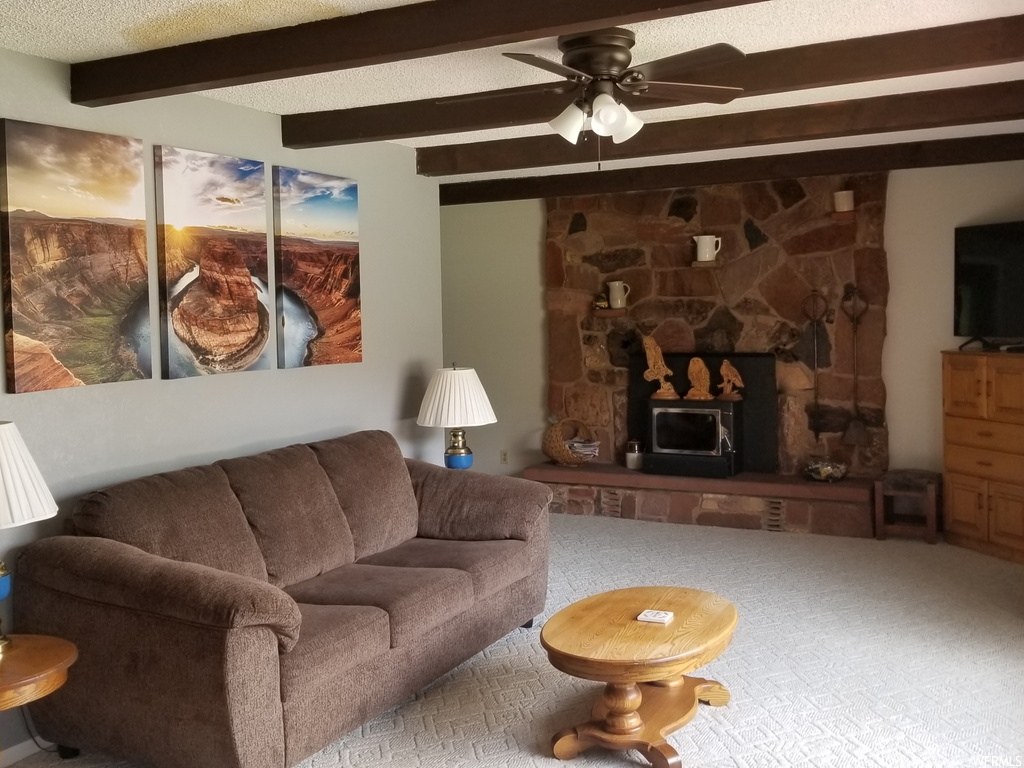 carpeted living room featuring a fireplace, a ceiling fan, beamed ceiling, and TV
