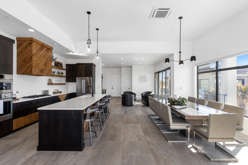 kitchen featuring a breakfast bar area, natural light, refrigerator, stainless steel double oven, dark brown cabinets, pendant lighting, light countertops, and light hardwood floors