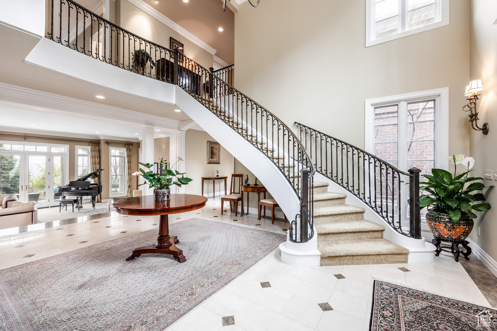 Stairs with ornamental molding, a high ceiling, light tile floors, and decorative columns